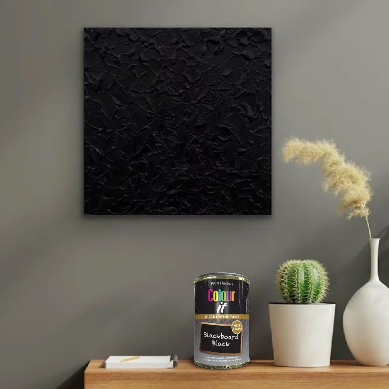 Tin of Blackboard Paint Black 300ml next to textured black artwork on grey wall