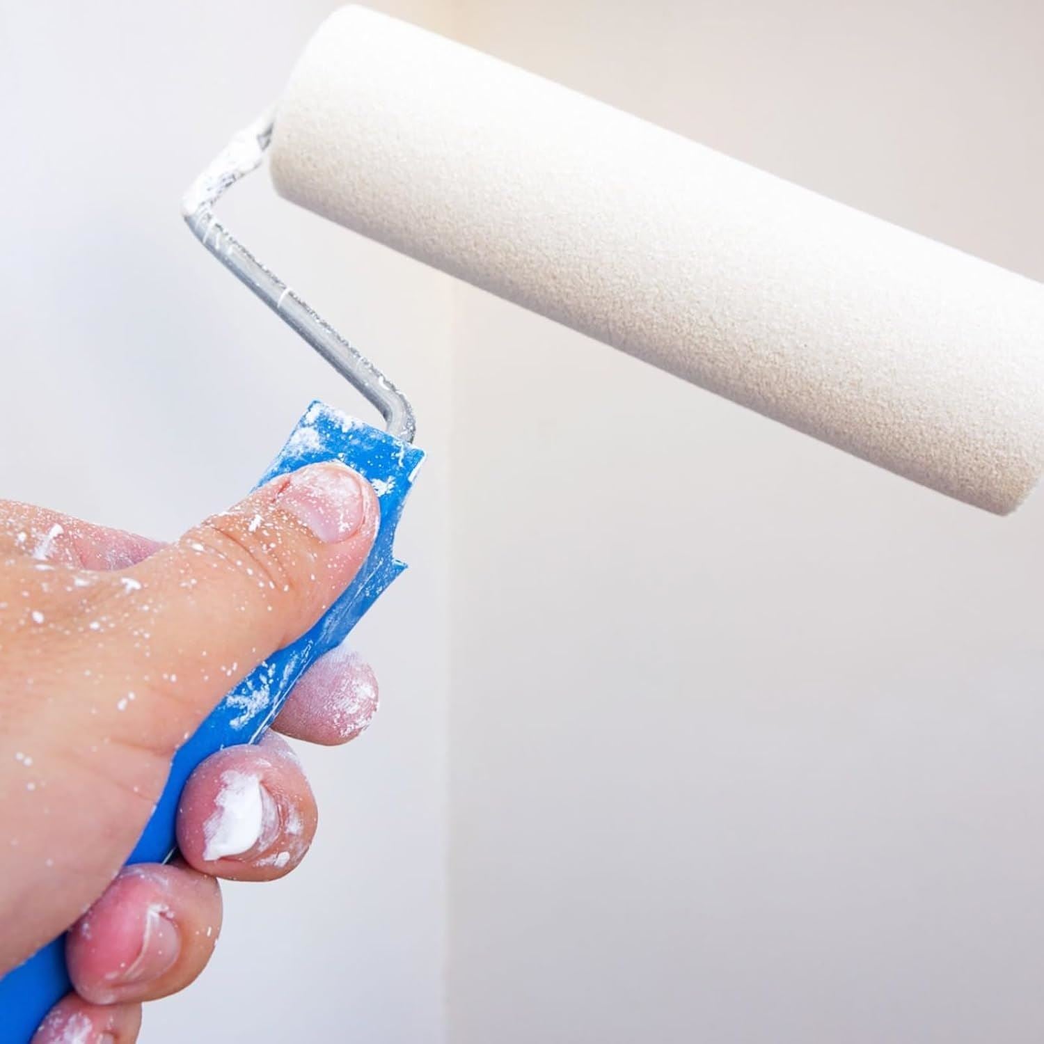 Hand holding a paint roller with white matt undercoat paint 300ml for smooth wall finishes